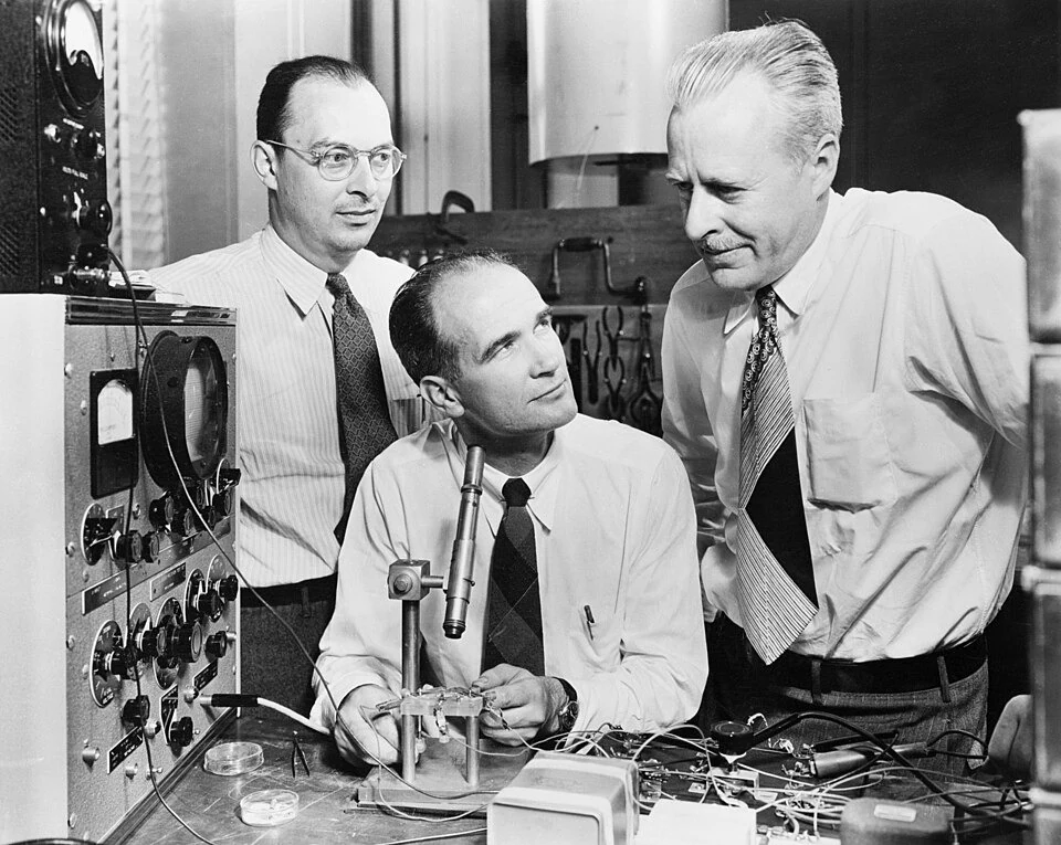 Three researchers at Bell Labs, with Shockley seated at a microscope